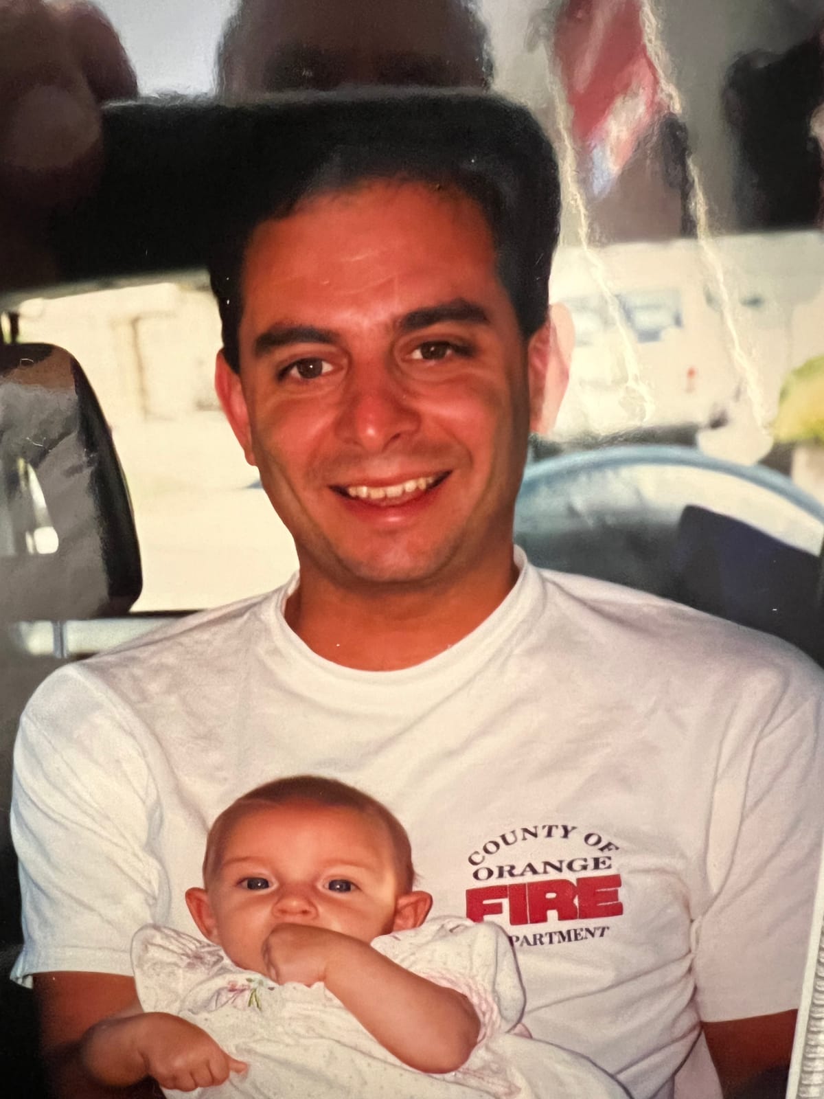 Lee Kulick during his years as a firefighter, wearing a County of Orange Fire Department shirt and holding his infant child